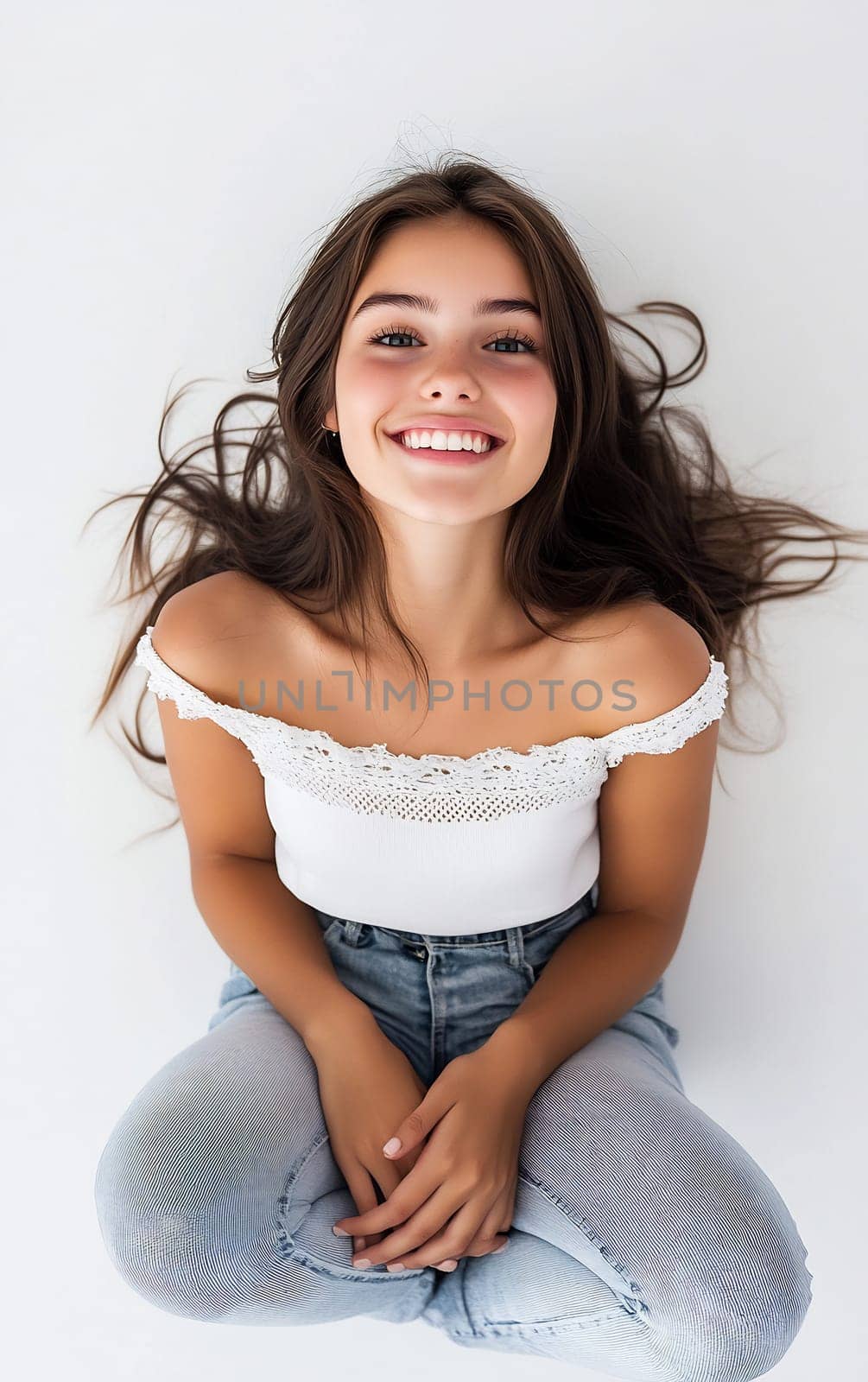 A cheerful woman with long hair sits on a light background, smiling while wearing casual attire. Her joyful expression radiates happiness.