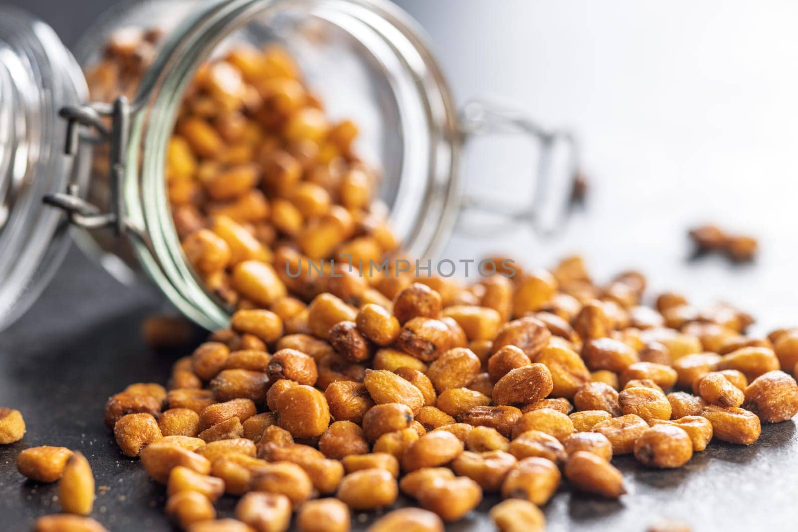 Roasted salted corn snack in jar on a black table.