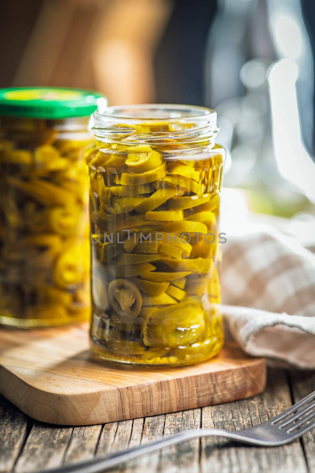 Pickled sliced jalapeno peppers in jar on a wooden table.