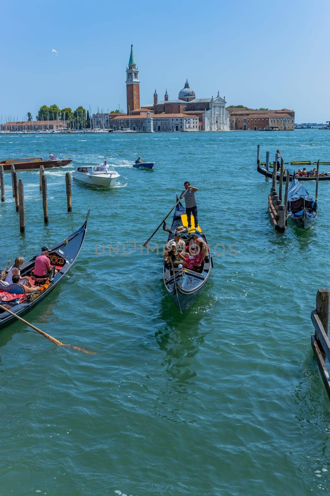Venice, Italy - July 26, 2024: Gondolas against the San Giorgio island in Venice, Italy. Gondola is the most attractive tourist transport in Venice. Traveling and vacation in sunny Venice.