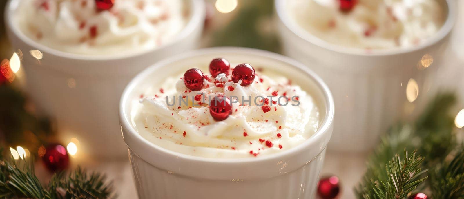 Creamy dessert topped with whipped cream and red sprinkles sits among holiday decorations creating a cozy Christmas atmosphere.