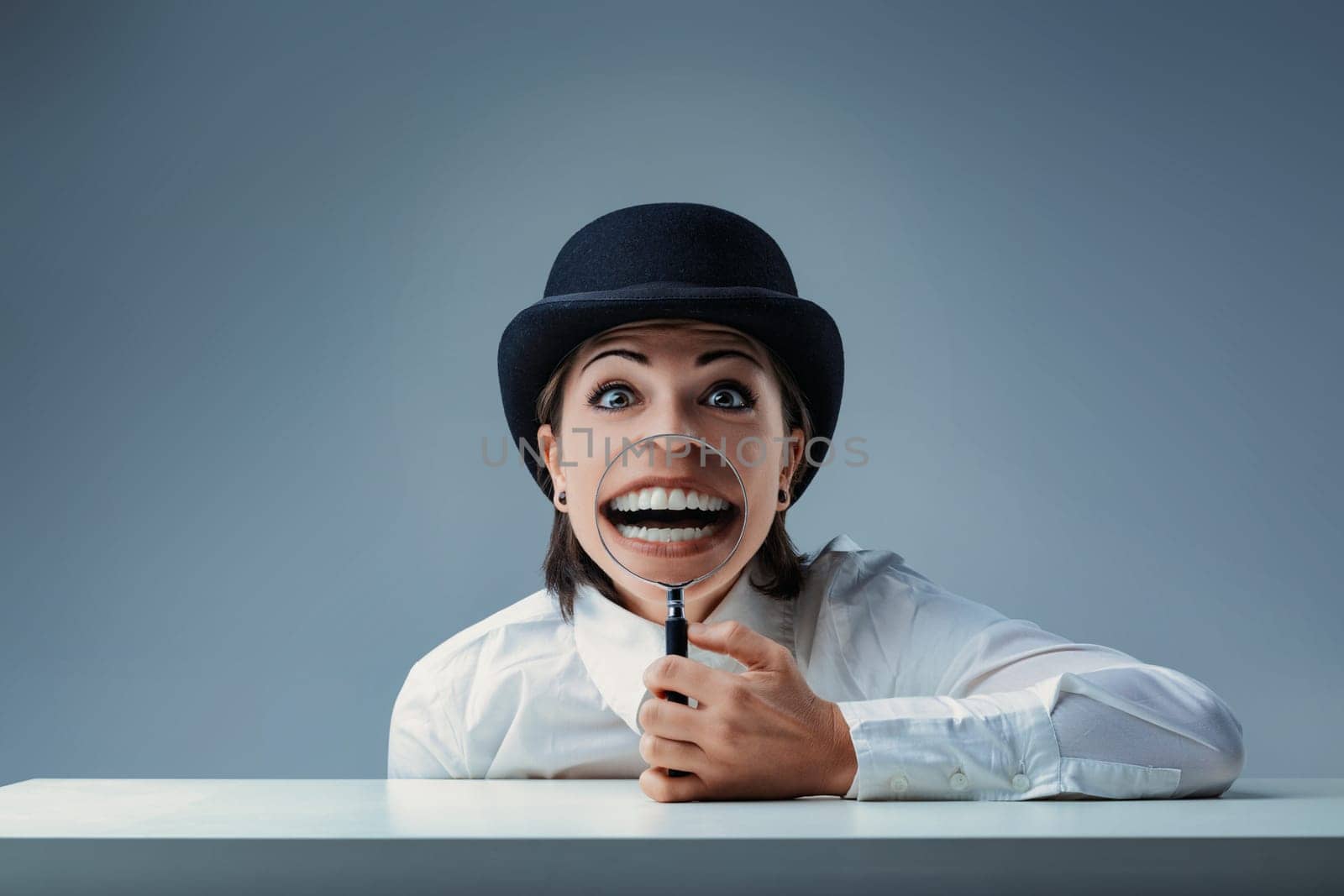 Young businesswoman in a bowler hat smiles with a magnifying glass, creating a comically large grin