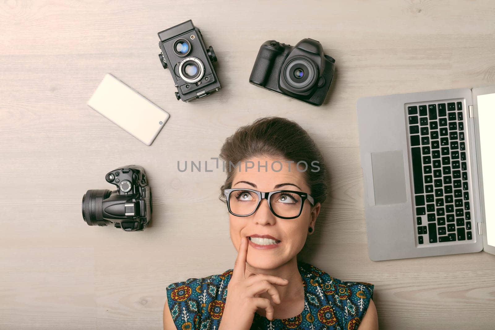 Young photographer lies on the floor, deep in thought, surrounded by camera and laptop, planning her next shoot with determination and creativity