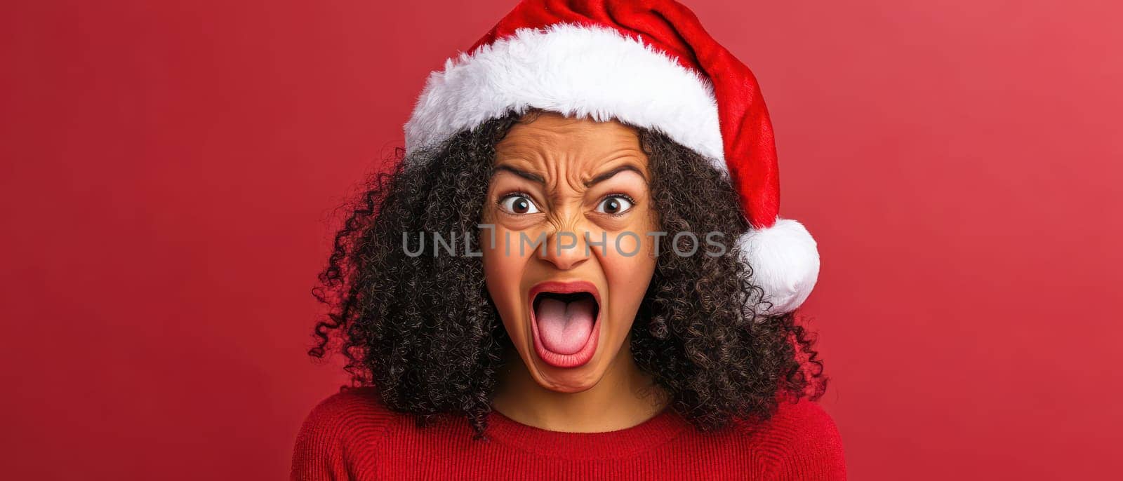 A person wearing a red Christmas hat expresses excitement with a wide open mouth in a joyful festive atmosphere against a red background.