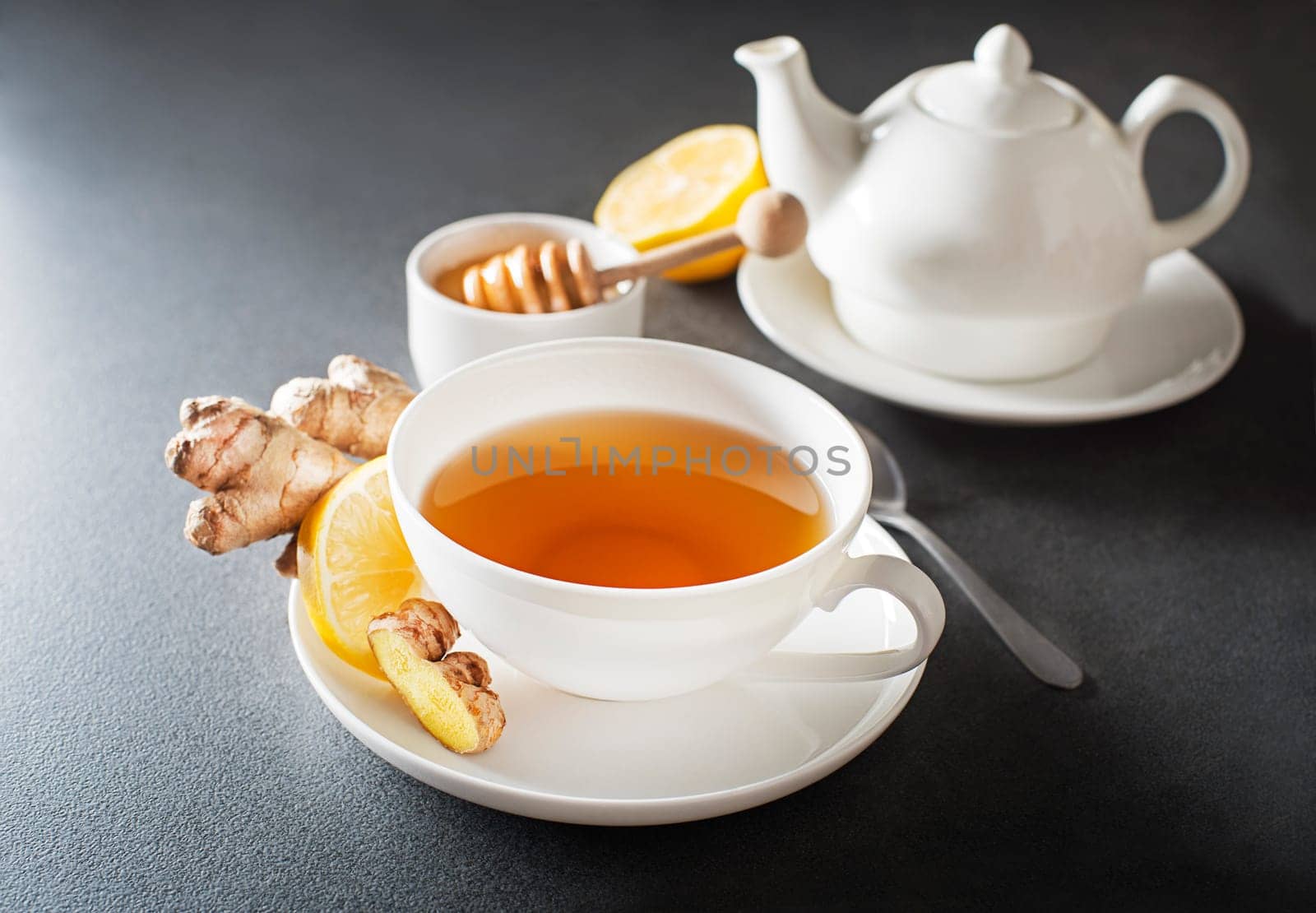 Cup of hot ginger tea with fresh ginger root and lemon on grey background close up