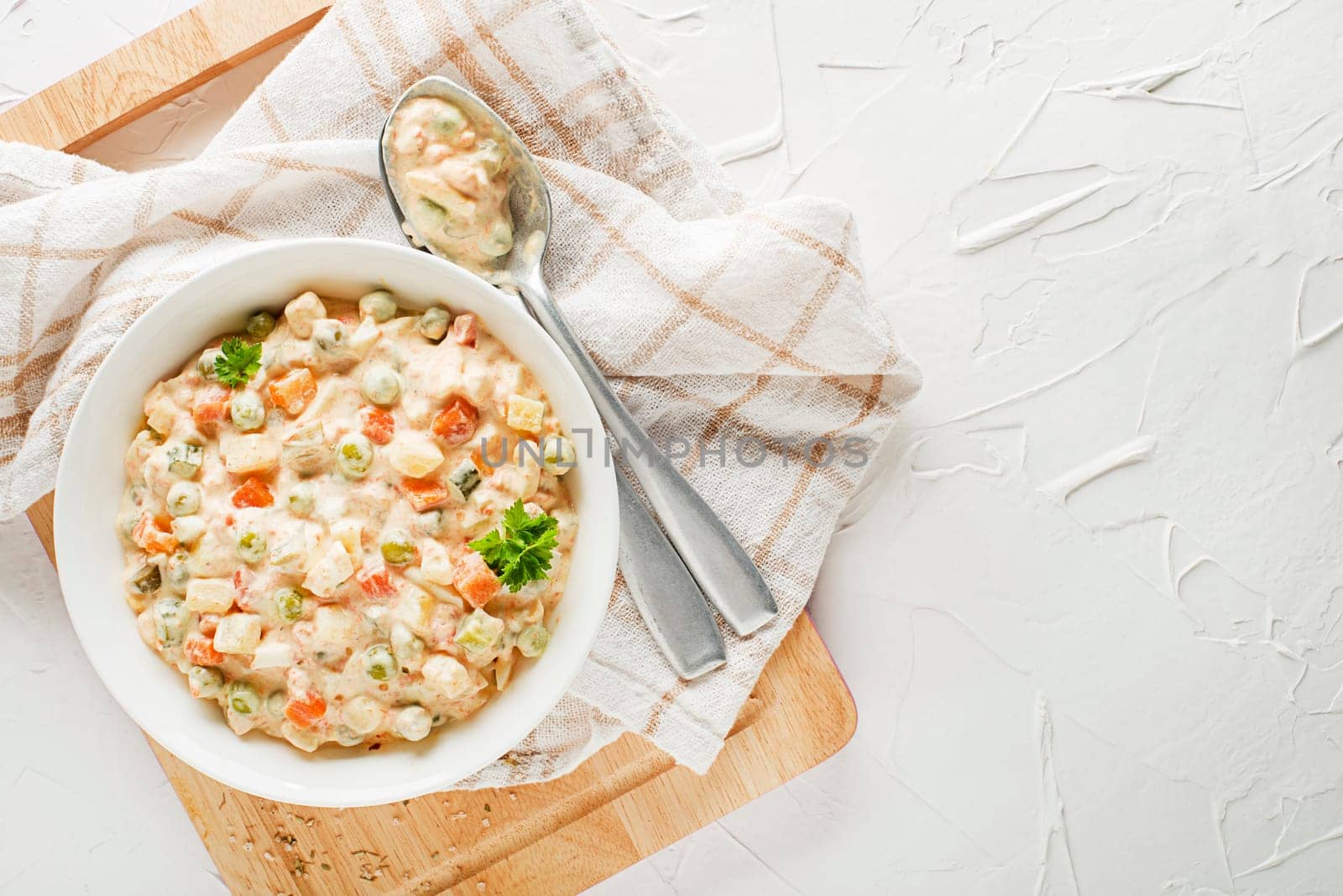 Bowl of russian salad or olivier or french salad with vegetables and egg dressed with mayonnaise on white table close up