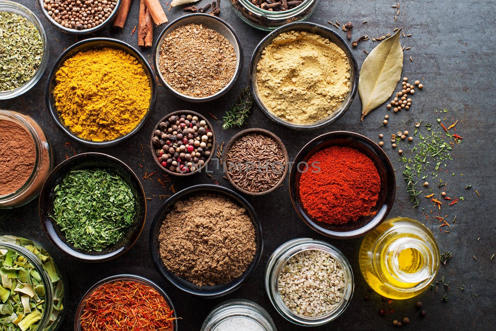 Colorful herbs and spices for cooking dishes. Indian and Asian spices. On grey stone background. Top view.