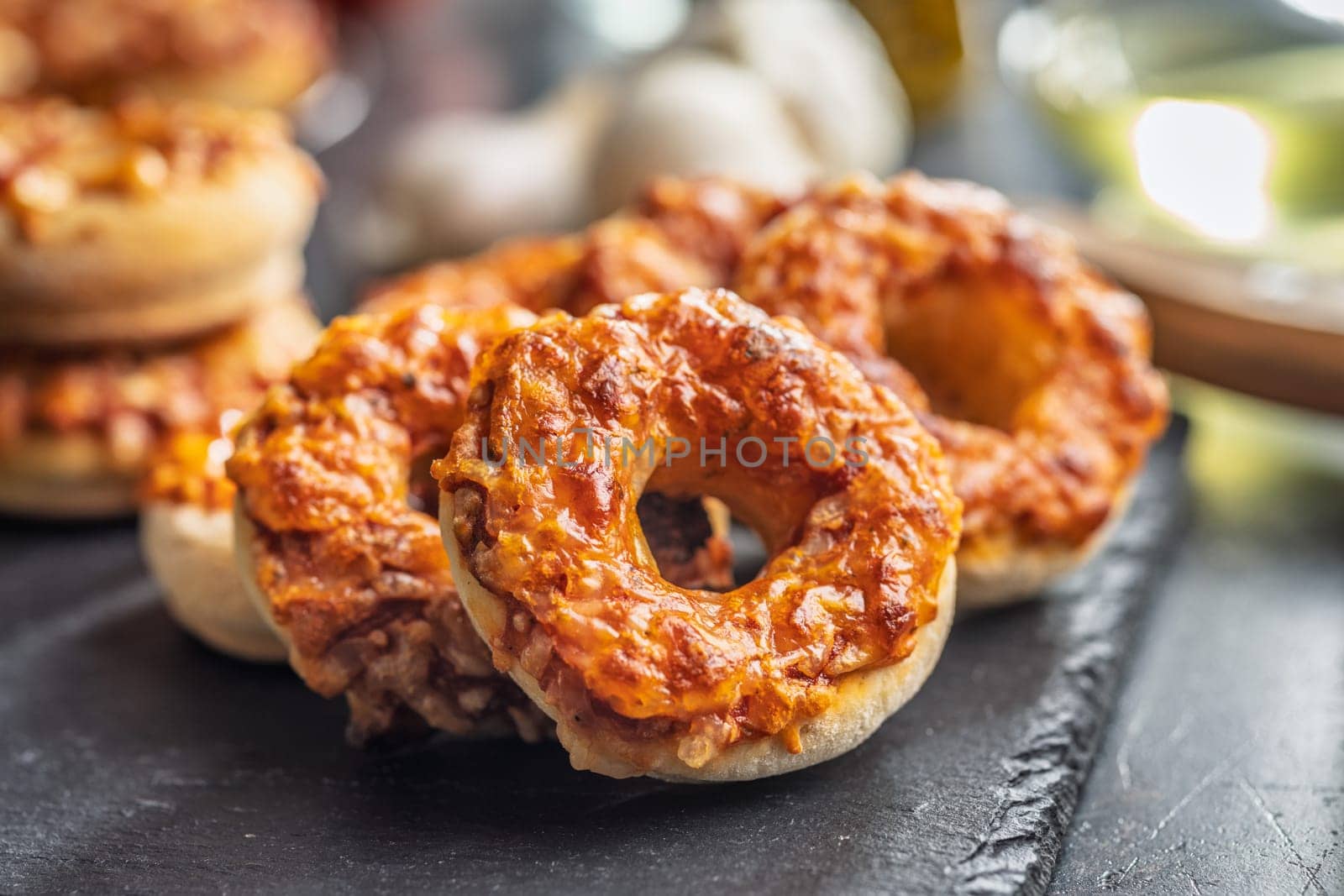 Mini pizza bagels on cutting board on a black table.