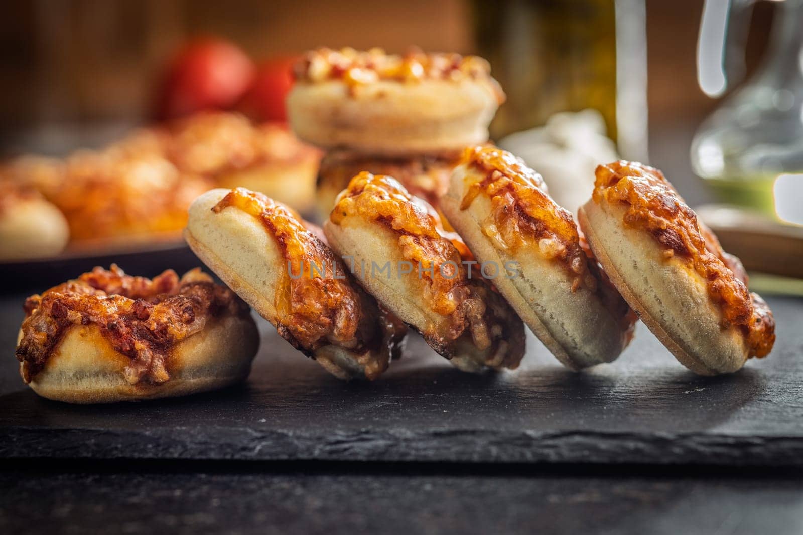 Mini pizza bagels on cutting board on a black table.