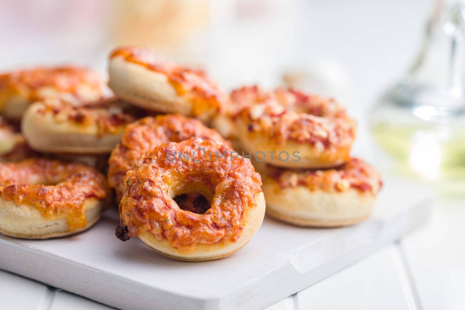 Mini pizza bagels on cutting board on a white table.