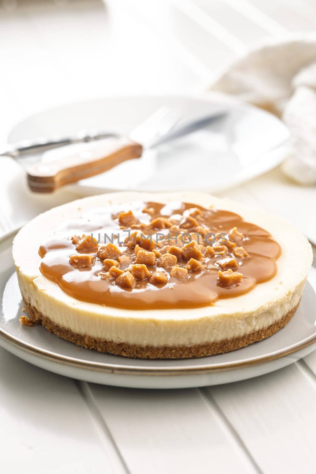 Cheesecake with caramel topping on plate on a white table.