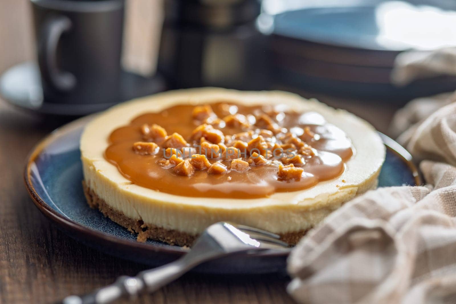 Cheesecake with caramel topping on plate on a wooden table.