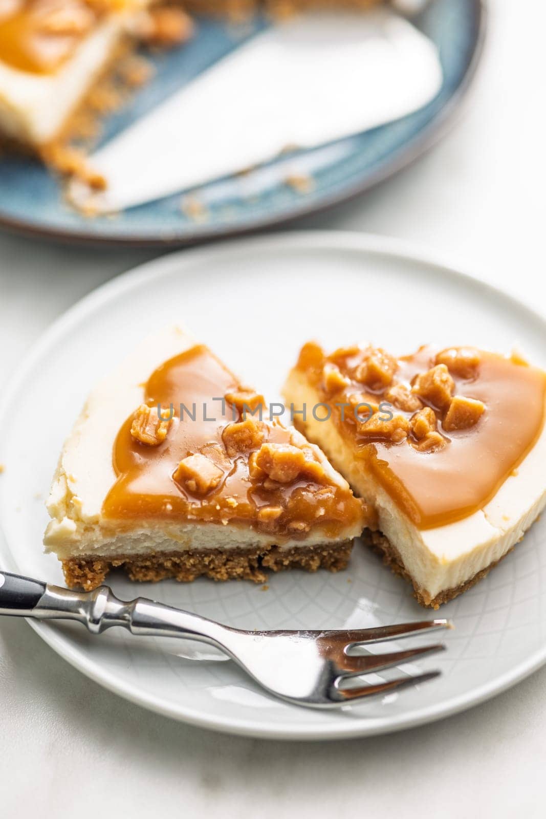 A cut piece of  cheesecake with caramel topping on plate on a kitchen table.