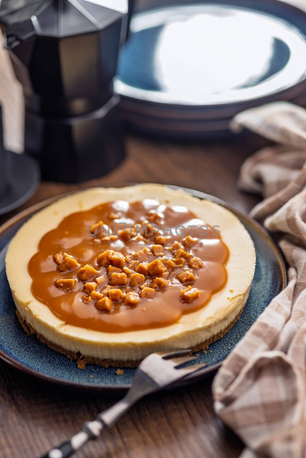 Cheesecake with caramel topping on plate on a wooden table.