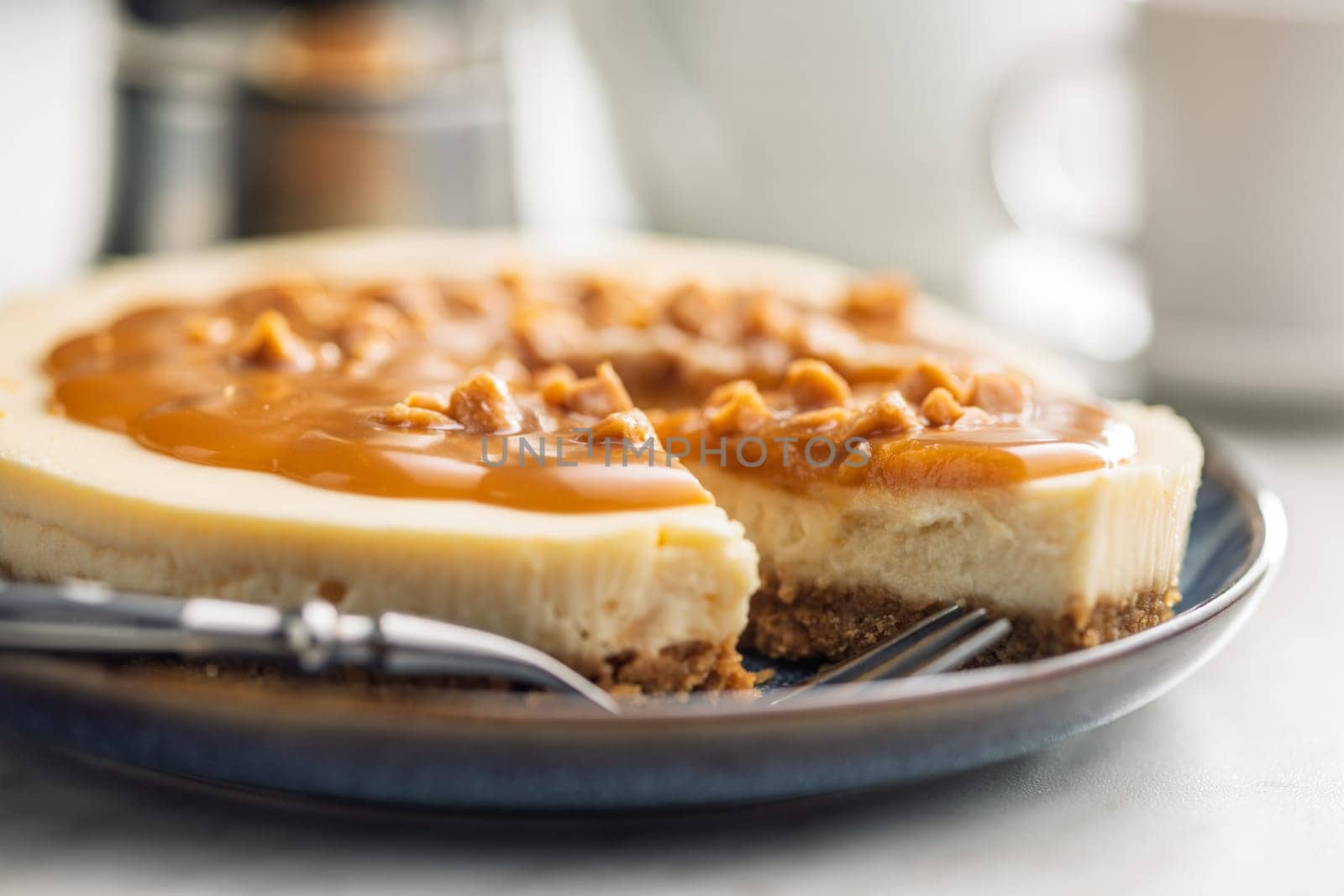 A cut piece of  cheesecake with caramel topping on plate on a kitchen table.