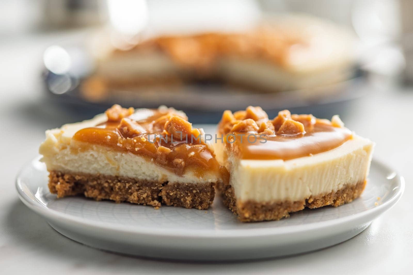 A cut piece of  cheesecake with caramel topping on plate on a kitchen table.