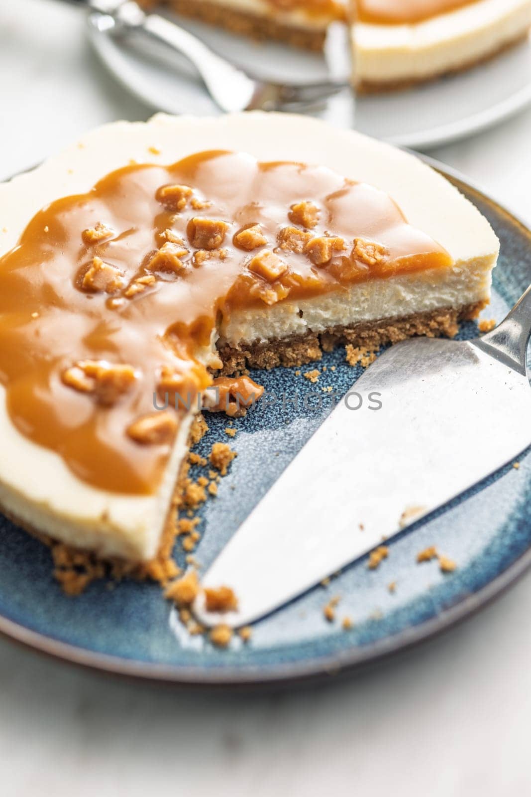 A cut piece of  cheesecake with caramel topping on plate on a kitchen table.