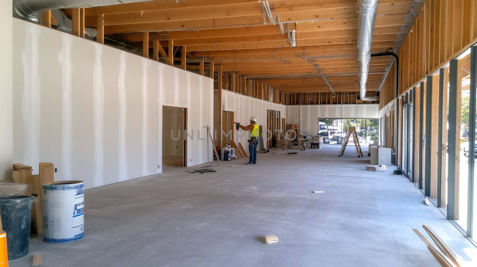 A construction worker evaluates progress in a large, unfinished interior space with exposed beams.