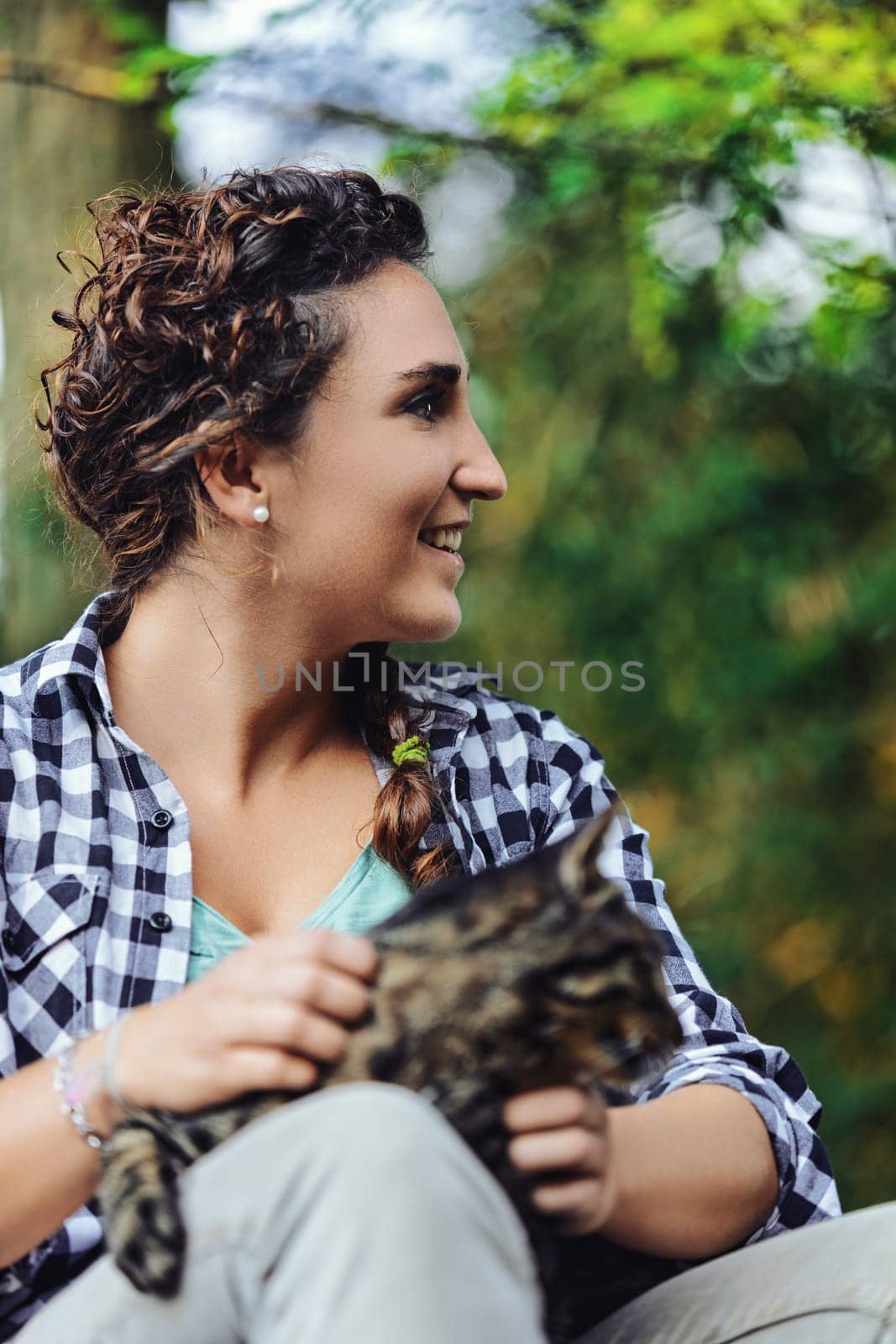 Young woman sits in the peaceful woods, holding her tabby cat, smiling serenely, surrounded by nature's beauty