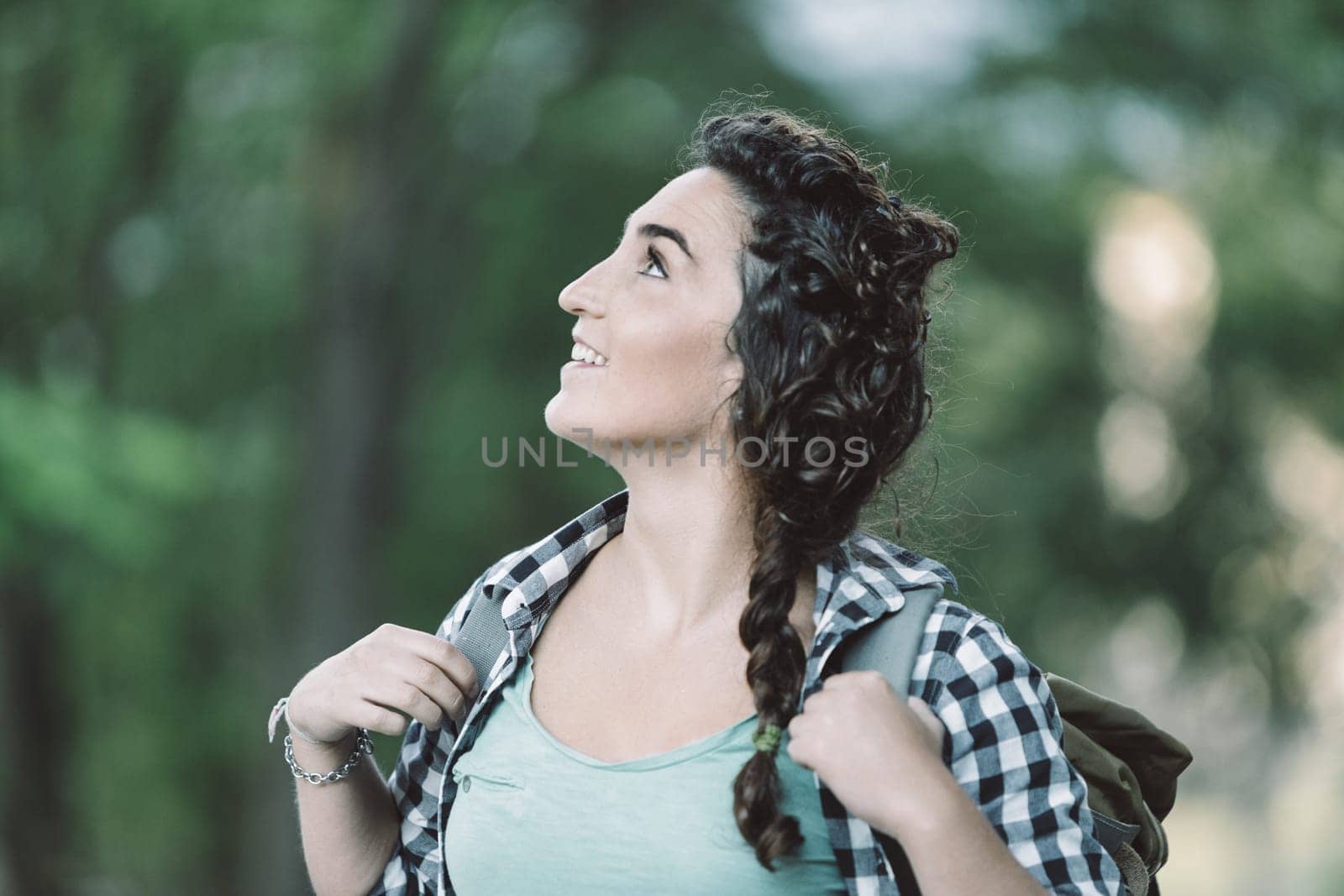 Young woman instructor with backpack smiling and looking up during a lesson in a forest, passing on knowledge to others in a beautiful natural environment