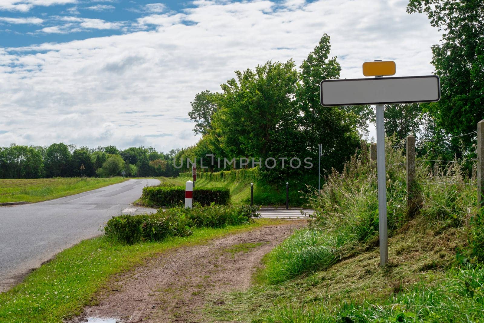 A road with an empty sign. The road is surrounded by trees and grass, Normandy, France
