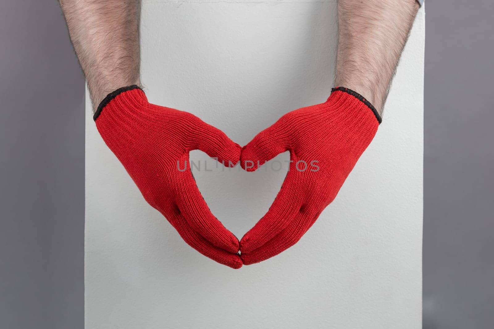 Close-up of hands wearing red gloves creating a heart shape against a gray sweater, symbolizing love, and care.