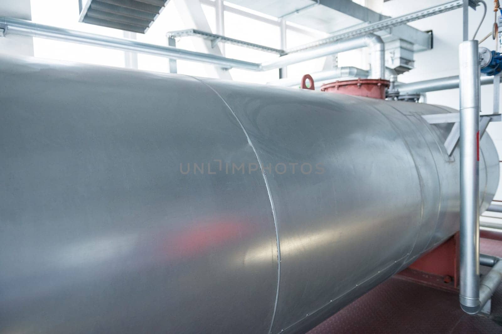 Outdoor Atmospheric Pressure deaerator. Close-up of a large metallic tank in an industrial facility, featuring pipes and equipment.
