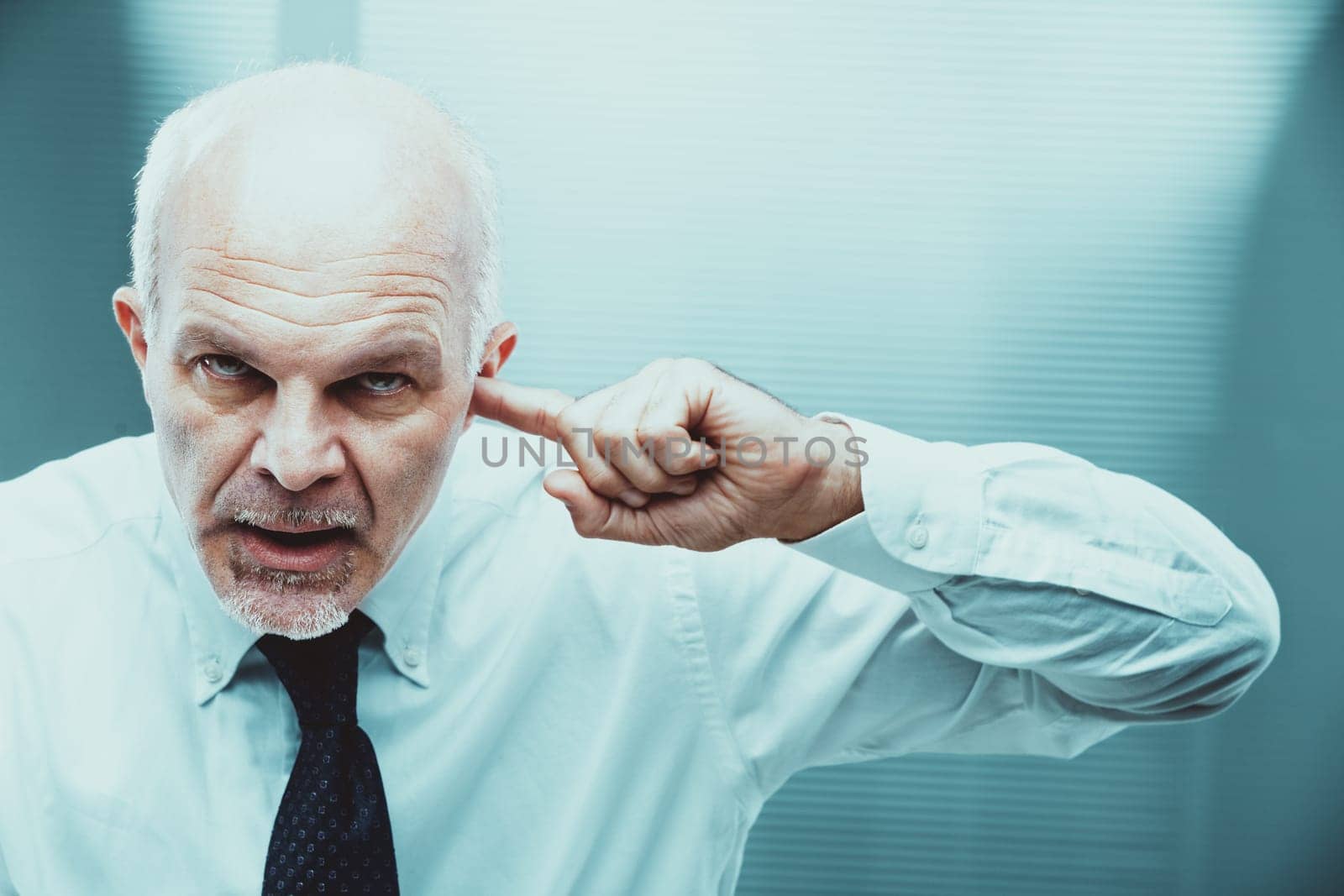 Stressed senior business manager plugging ears with fingers while shouting in disagreement, expressing frustration and anger over a conflict at work in a corporate office setting