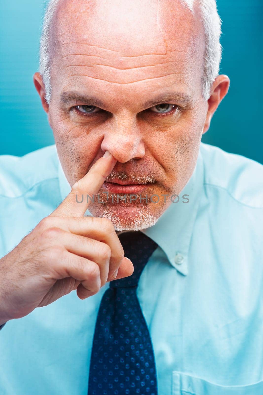 Close-up portrait of a mature businessman humorously picking his nose with his finger, showcasing a funny and irreverent gesture that highlights bad manners in a corporate setting
