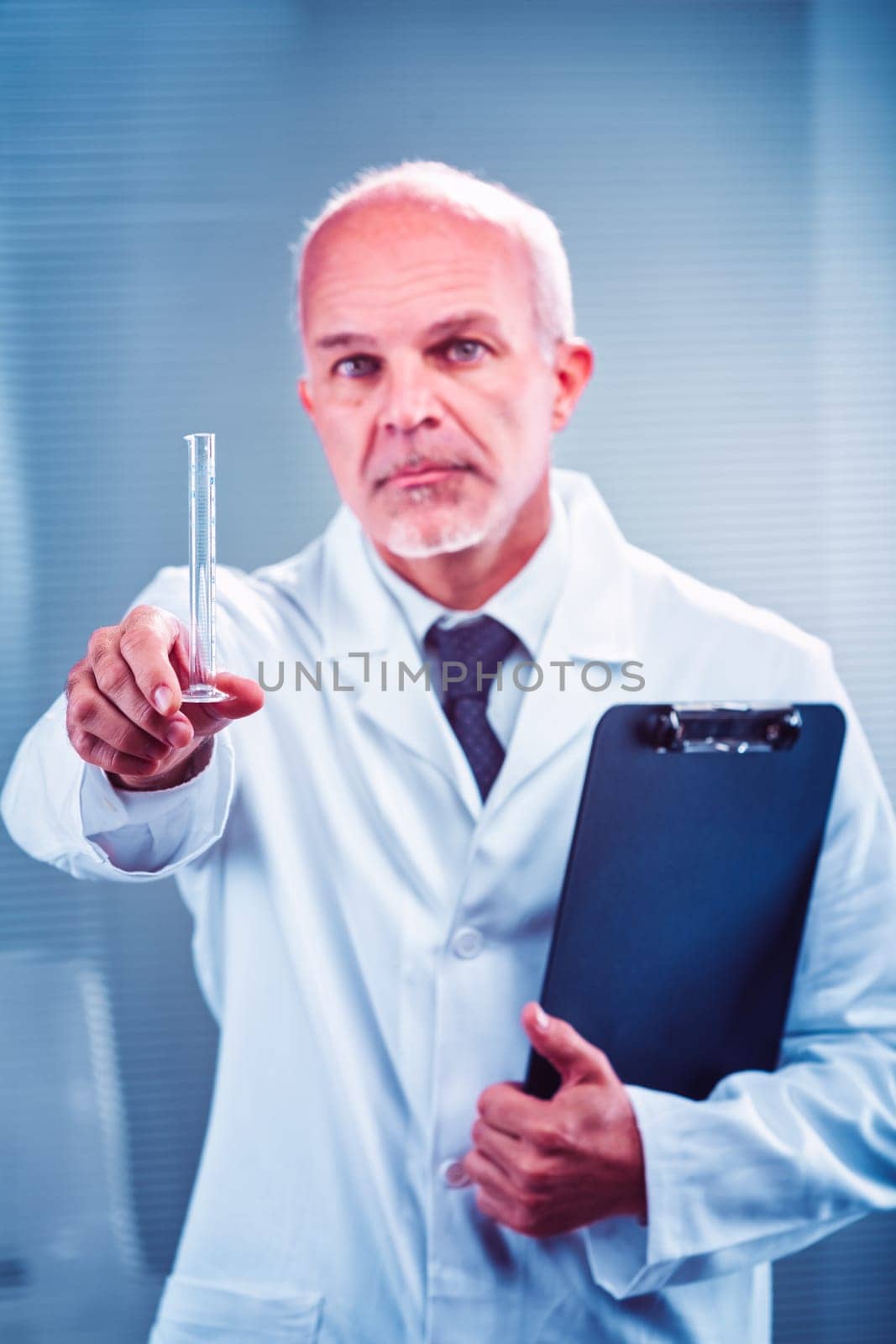 Senior male scientist wearing a lab coat, holding a clipboard and showing a test tube in a laboratory setting, conducting detailed scientific research and analysis
