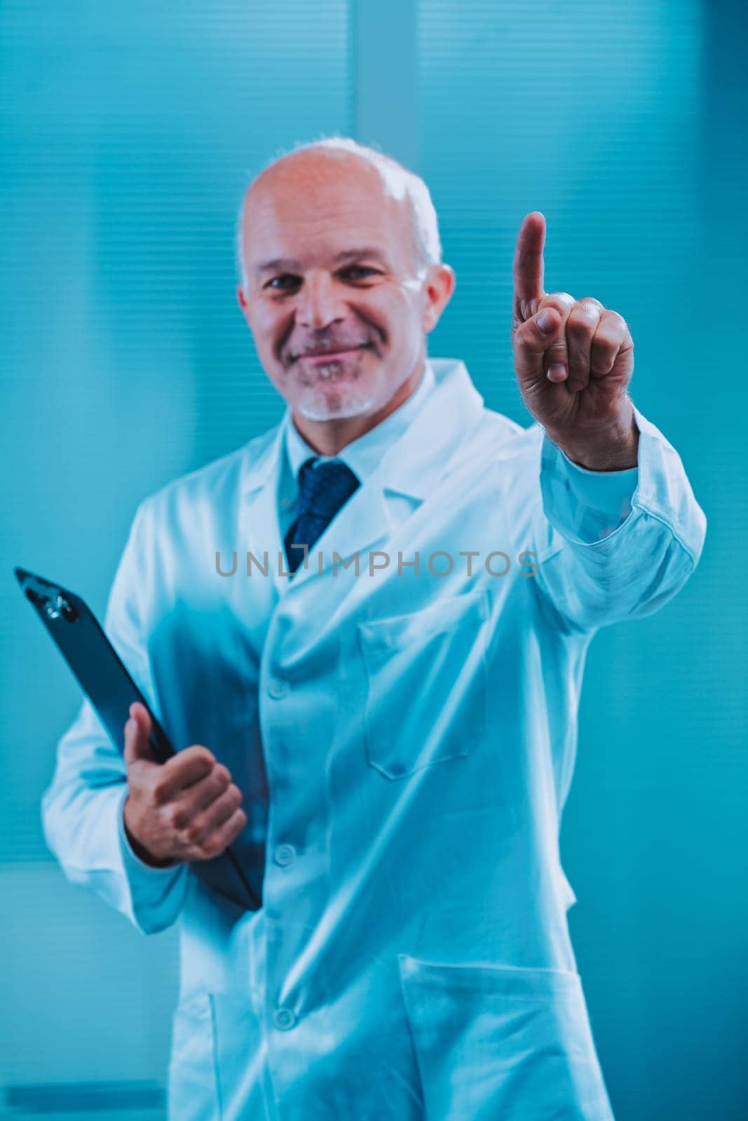 Mature male doctor wearing a lab coat is holding a clipboard and pointing his index finger upwards, signifying an important medical instruction or recommendation