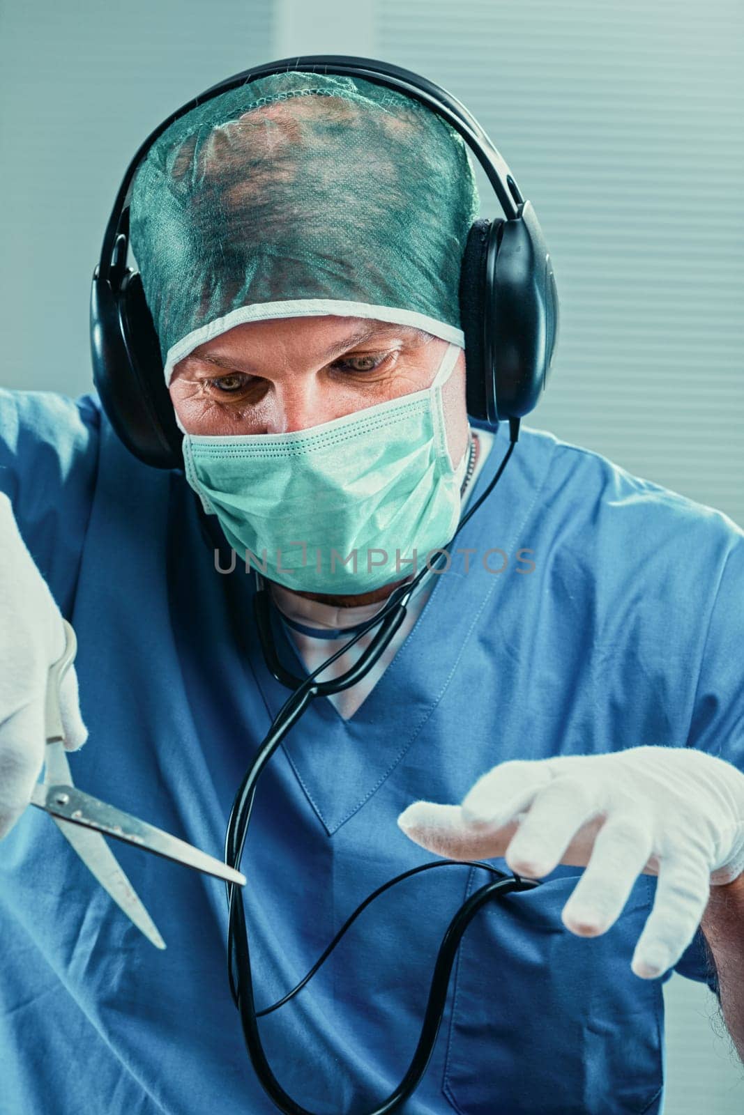 Surgeon wearing surgical mask, cap, gloves and scrubs listens to music with headphones while holding surgical scissors, showcasing a blend of focus and relaxation before a medical procedure