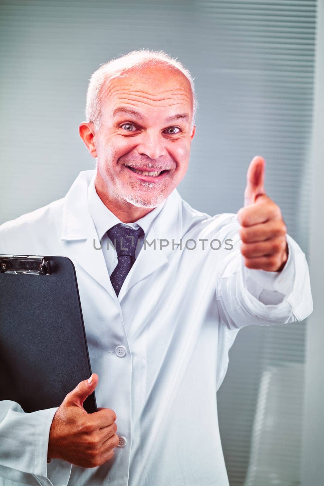 Mature, male doctor is smiling and giving a thumbs up gesture while holding a clipboard, expressing confidence and positive outcome in healthcare