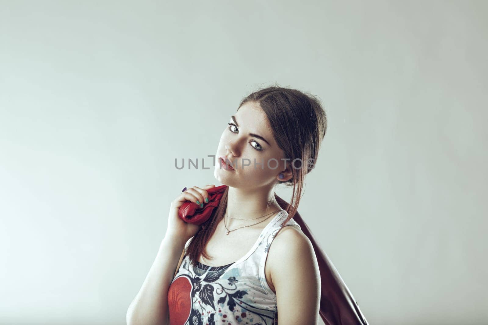 Portrait of a fashionable young woman holding a red leather jacket over her shoulder, looking confidently at the camera against a light gray background