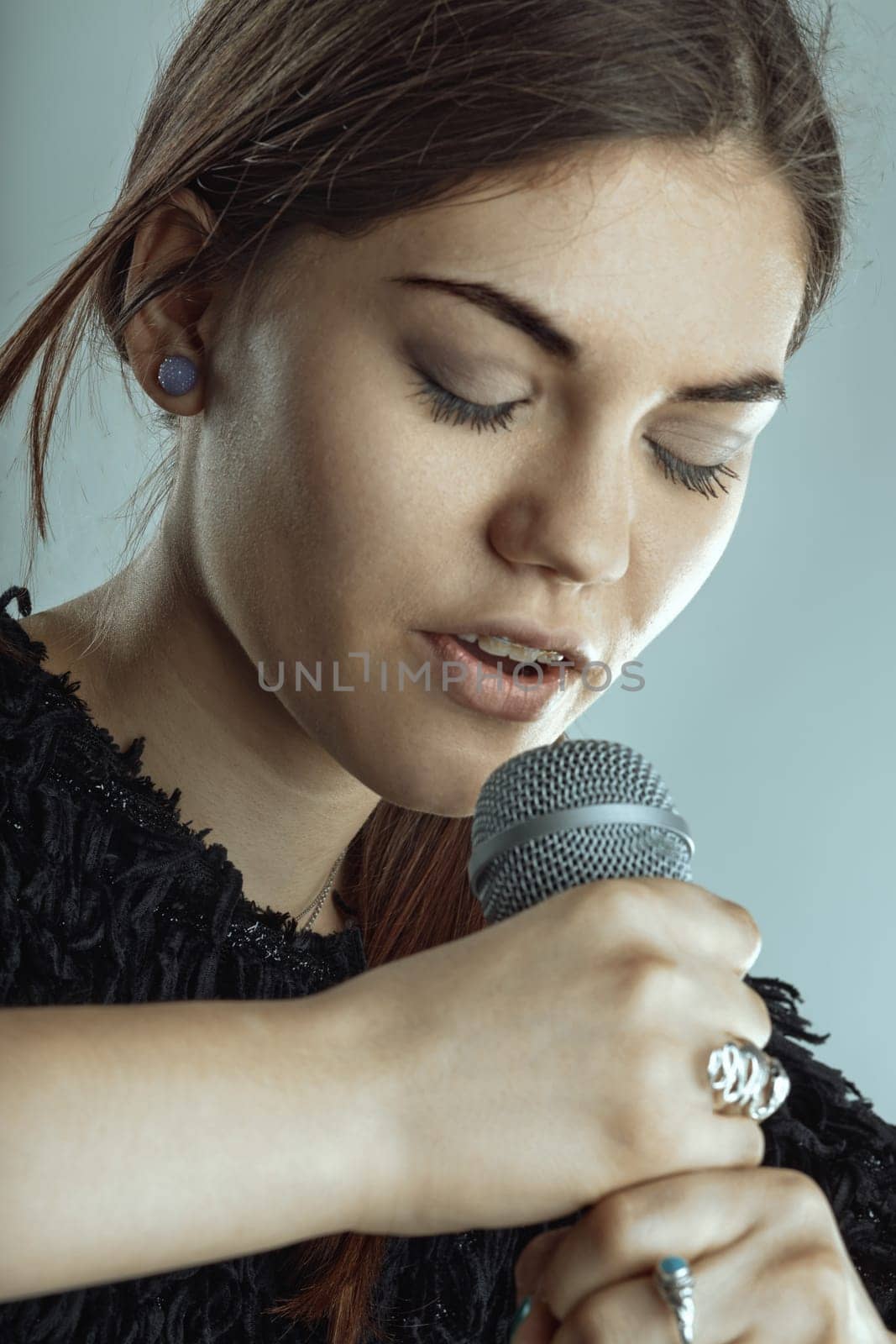 Young woman singing passionately into a microphone, eyes closed, fully immersed in the emotion of her performance. Capturing the essence of music and artistry on stage