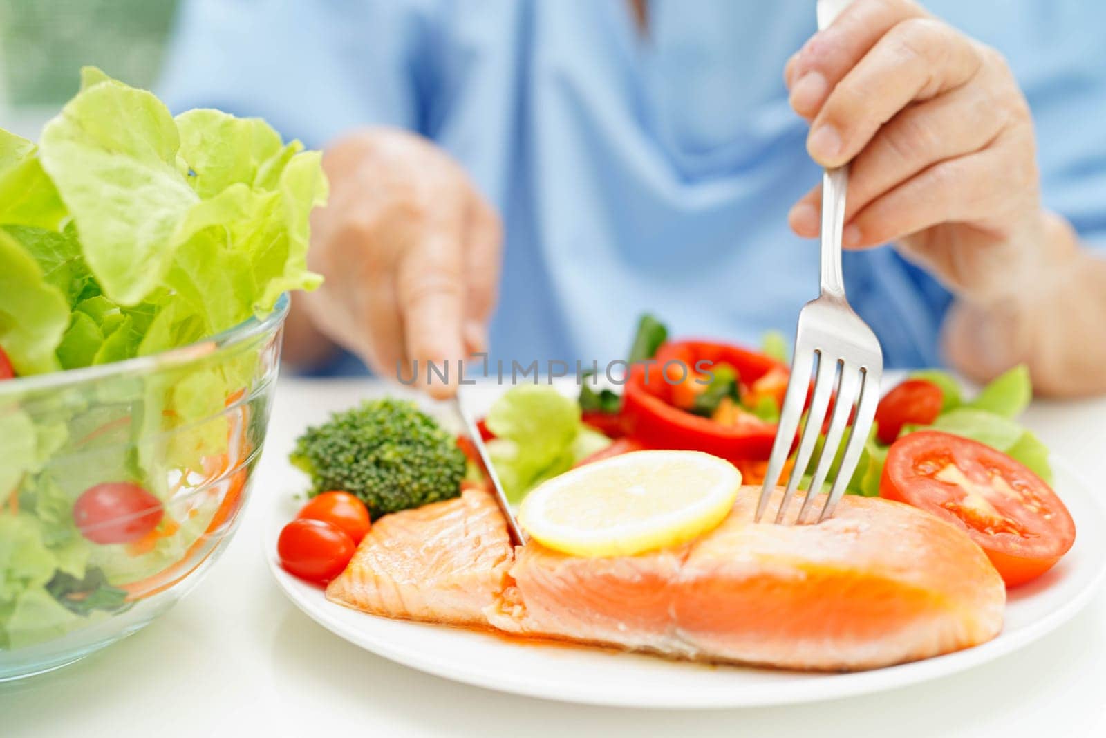 Asian elderly woman patient eating salmon stake and vegetable salad for healthy food in hospital.