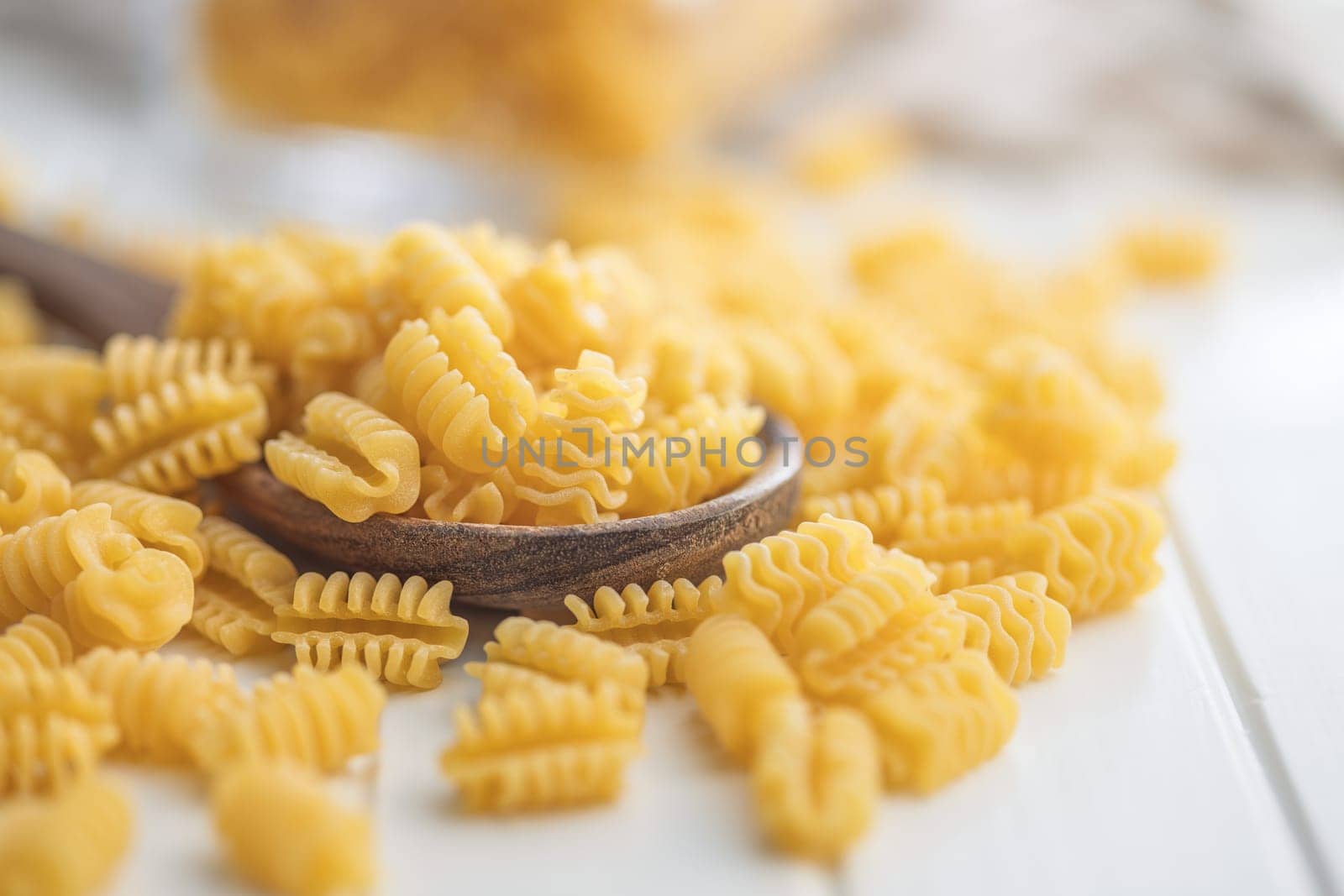 Uncooked italian pasta. Radiatori pasta in spoon on a white table.