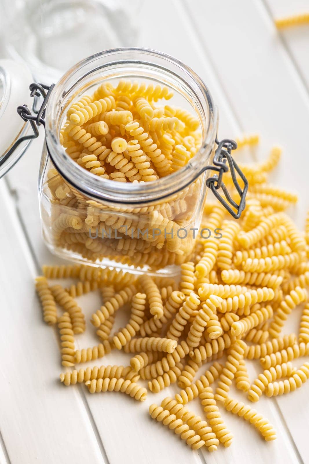 Uncooked italian pasta. Fusilli pasta in jar on a white table.