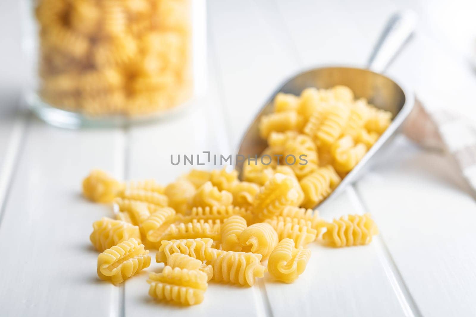 Uncooked italian pasta. Radiatori pasta in scoop on a white table.