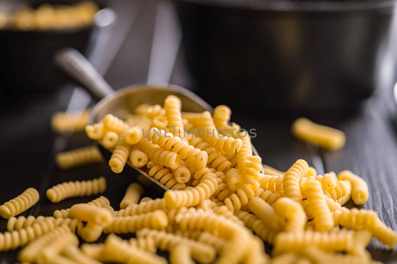 Uncooked italian pasta. Fusilli pasta in scoop on a black table.