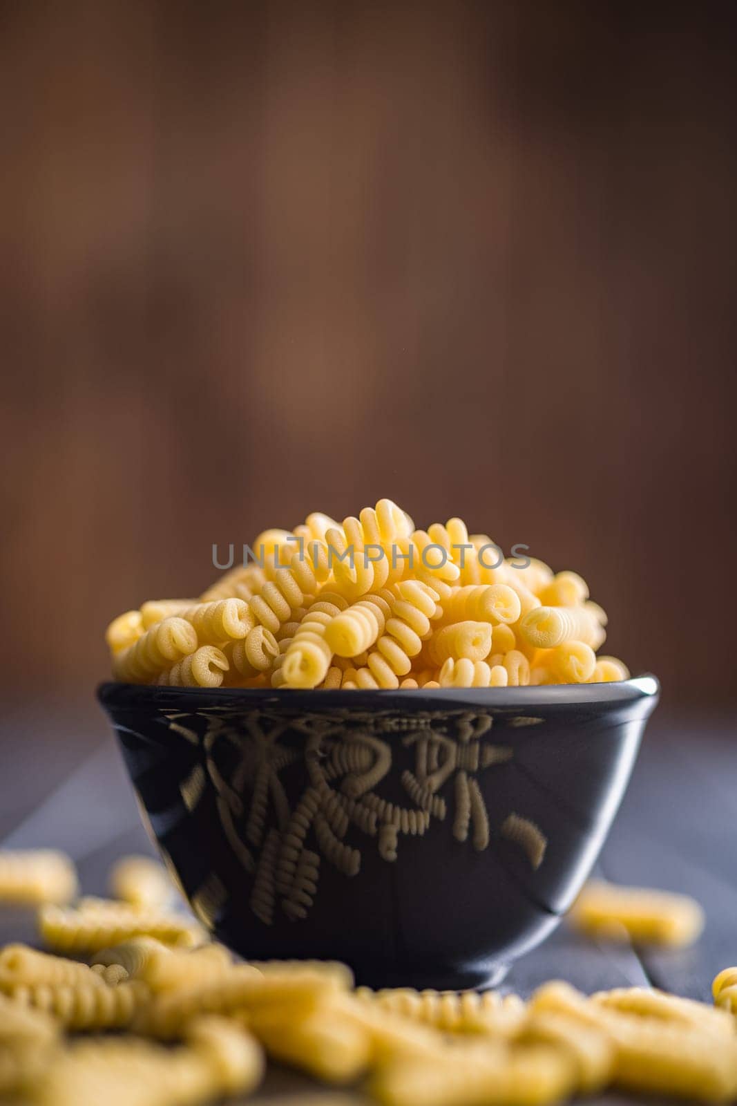 Uncooked italian pasta. Fusilli pasta in bowl on a black table.