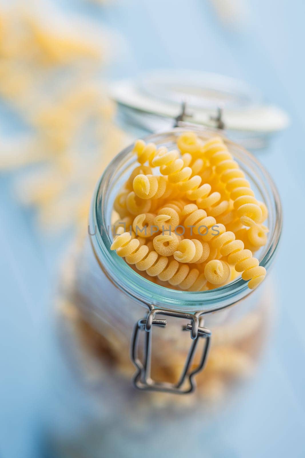 Uncooked italian pasta. Fusilli pasta in jar on a blue table.