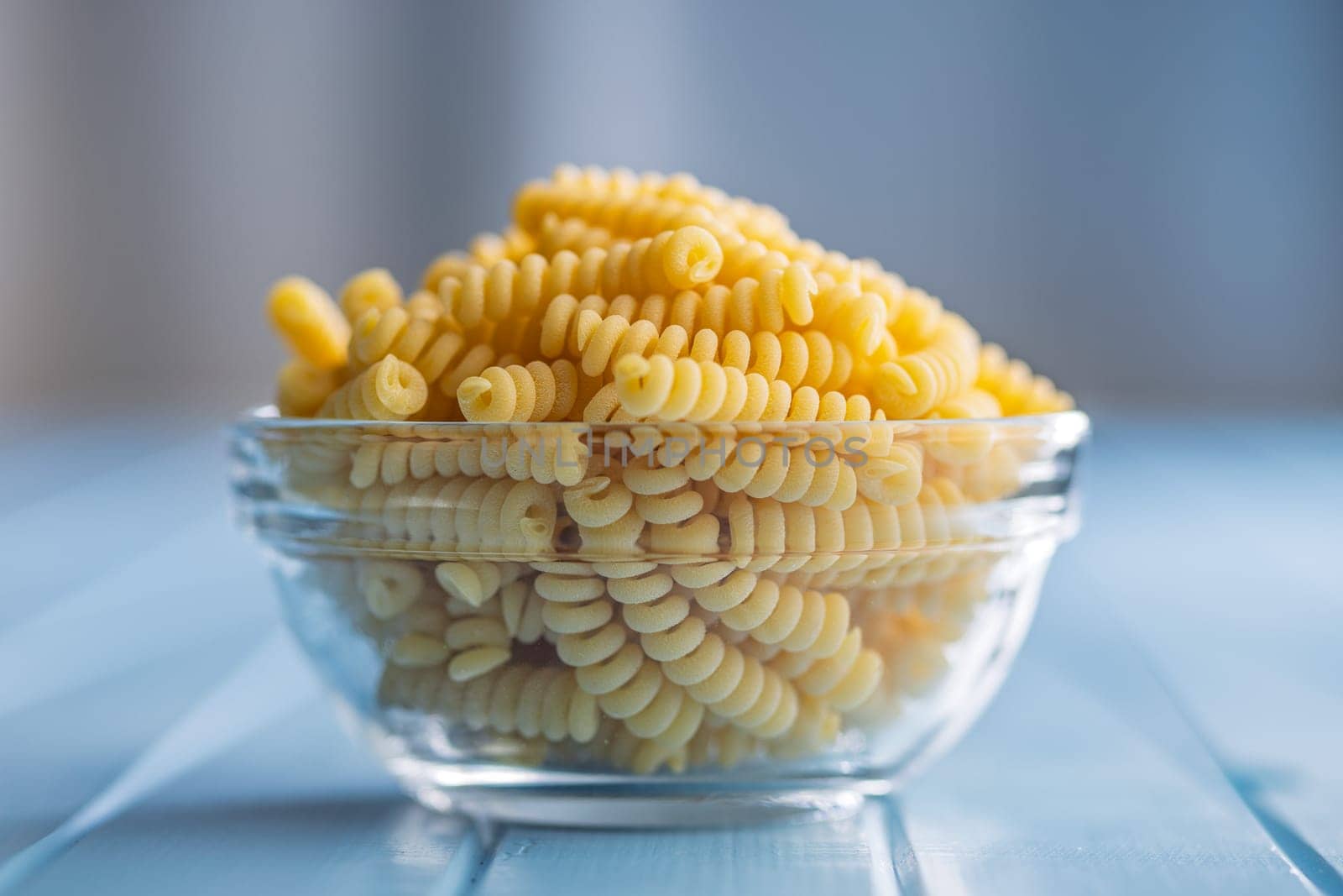Uncooked italian pasta. Fusilli pasta in bowl on a blue table.