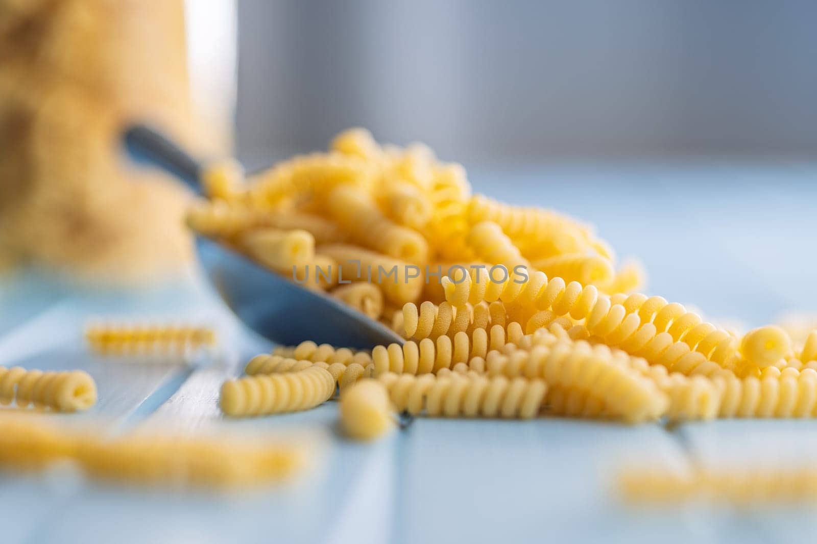 Uncooked italian pasta. Fusilli pasta in scoop on a blue table.