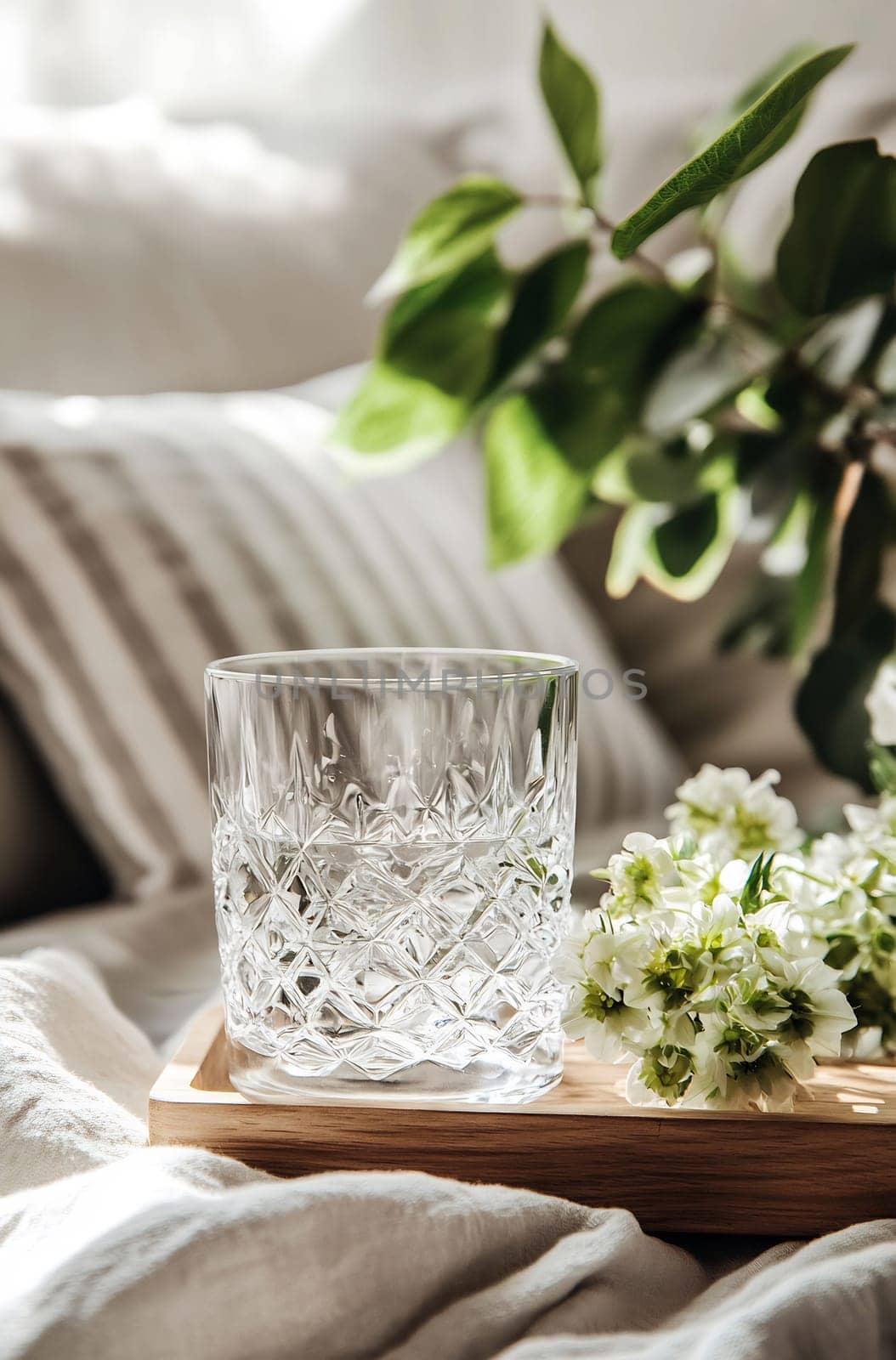 A crystal glass rests on a wooden tray beside fresh flowers in a bright and comfortable setting, creating a serene atmosphere.