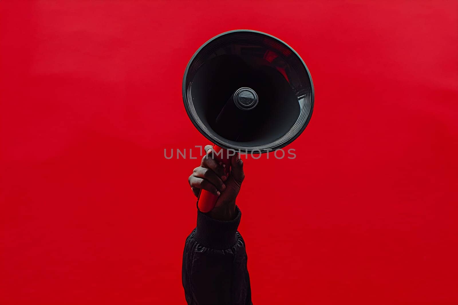 A hand holds a megaphone high against a vibrant red background, representing empowerment and activism during a passionate moment.