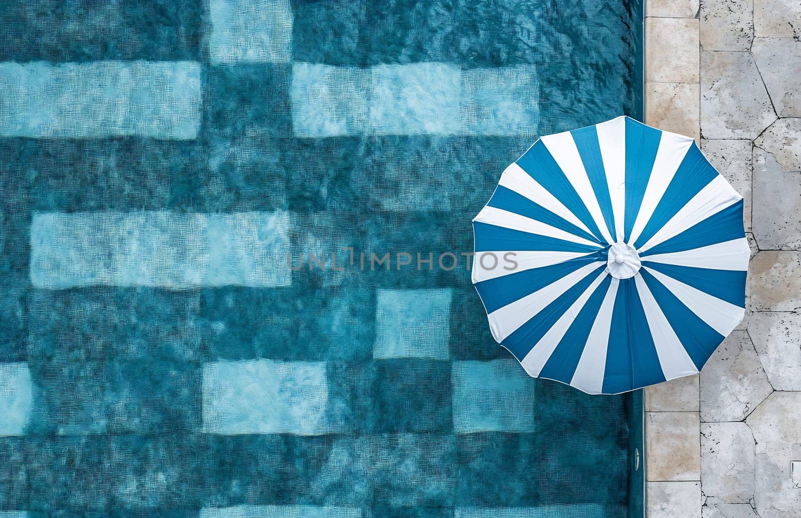A striped umbrella shades a serene pool area with clear blue water and tiled flooring. Perfect for a peaceful retreat.