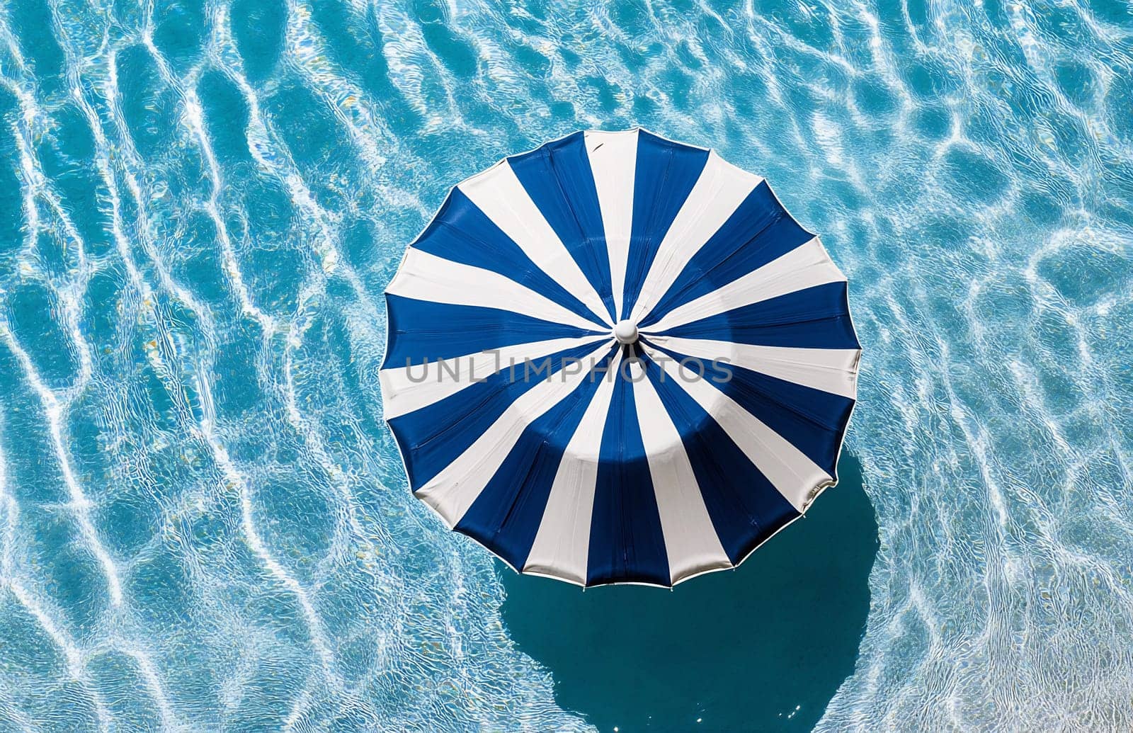 A striped beach umbrella floats above the shimmering blue water, creating a vibrant spot of shade on a sunny day.