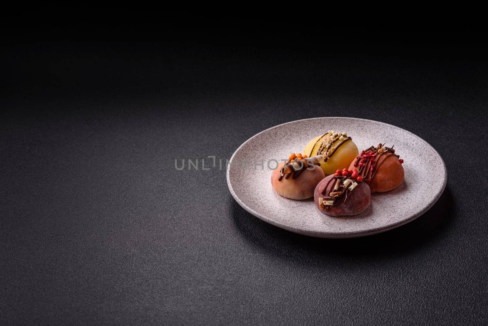 Delicious colorful asian mochi sweets with rice dough shell and fruit filling on dark concrete background