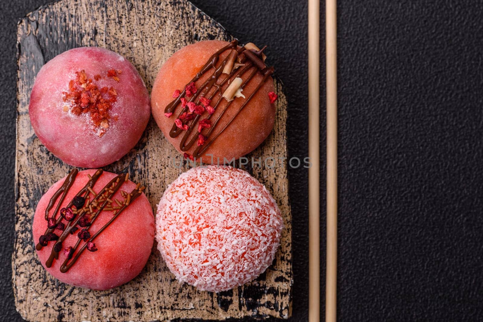 Delicious colorful asian mochi sweets with rice dough shell and fruit filling on dark concrete background